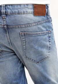 Faded blue denim jeans with a leather label, five-pocket design, stitched seams, and a slightly worn texture on the fabric.