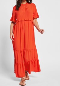 Robe maxi rouge avec de courtes manches volantes, présentant un design à plusieurs niveaux et une taille froncée. Fabriquée en tissu léger avec une texture lisse.