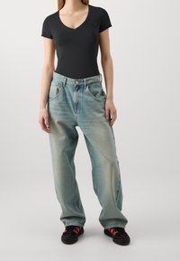 Černý krátký rukáv bodysuit s výstřihem do V, spárovaný s volnými, světle modrými vybledlými džíny a černými botami s červenými akcenty.