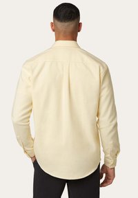 Gelbes Langarmhemd mit abgerundetem Saum und Knopfmanschetten. Aus weichem Material gefertigt, mit einer Rückenpasse und feiner Struktur.