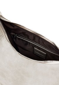 Helles graues Lederinnere der Tasche mit einem dunklen Futter, das eine Reißverschlusstasche und ein Etikett enthält. Glatte Textur mit metallischen Reißverschlussdetails.