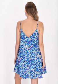 Abito azzurro senza maniche con un vivace motivo astratto in verde e rosa, caratterizzato da uno scollo a V sul retro e una gonna svasata con orlo scallop.