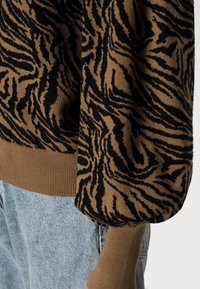 Brun tröja med ett svart tigerrandigt mönster, stickad textur och ribbad mudd, stylad med ljusblå jeans.