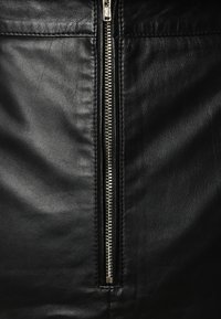 Černý kožený oděv s centrálním kovovým zipem, hladkým povrchem a pečlivě šitými švy po obou stranách zipu.