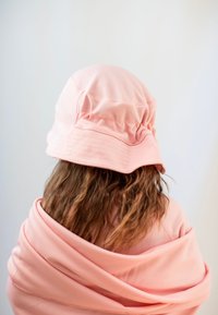 Rosa bucket hat med en texturerad tyg, bred brätte och samlad detalj, bärs med en matchande rosa scarf som hänger över axlarna.