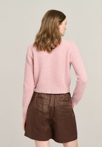 Helles rosa, gestricktes Sweatshirt mit einem verkürzten Design und geripptem Saum, kombiniert mit braunen Shorts, die seitliche Taschen und eine glatte Textur aufweisen.