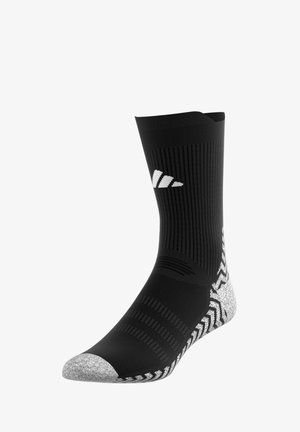 Chaussette de sport noire avec un design côtelé, orteil et talon argentés, présentant des accents texturés et un logo réfléchissant sur le tibia.