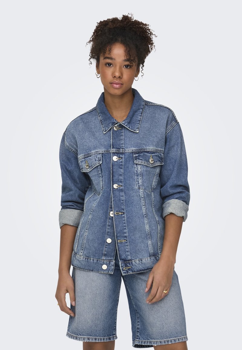 Chaqueta de mezclilla en azul claro con cierre de botones, dos bolsillos en el pecho y mangas enrolladas. Combinada con unos pantalones cortos de mezclilla a juego.