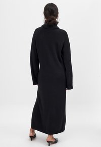 Vestito maglione nero a maglia con colletto alto, maniche lunghe e polsini a coste, caratterizzato da una silhouette lunga e morbida e un tessuto texturizzato.