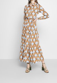 Robe longue à motif floral avec des nuances de bleu et d'orange, dotée d'un col, de manches longues et d'une taille ceinturée pour une silhouette ajustée.