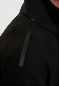 Sort sweatshirt med høj krave, blød tekstur og en blank sort detalje langs skuldersømmen.