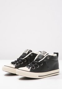 Czarne trampki typu high-top wykonane ze skóry, z białym futerkiem wewnątrz, czarnymi sznurówkami, oczkami oraz gumową podeszwą z kremowym noskiem.