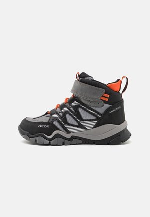 Zwart-grijze buitenlaarzen met een hoog model tot aan de enkels, klittenbandsluiting, oranje accenten en rubberen antislipzolen met structuur. Geox-logo zichtbaar.