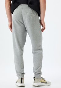Pantalones de chándal grises con un diseño ajustado, puños acanalados y un bolsillo trasero. Tejido suave con una textura lisa. Combinados con zapatillas deportivas.
