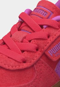 Φωτεινό κόκκινο σουέτ αθλητικό παπούτσι με παχιά κόκκινα κορδόνια και μωβ επένδυση στη γλώσσα, με μωβ λογότυπο Puma στο πλάι και στη γλώσσα.