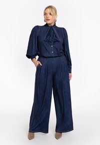 Donkerblauwe spijkeroutfit met een blouse met lange mouwen en strik, en wijde broek, verfraaid met gouden knopen en stikdetails.
