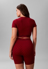 Rød mønstret to-delt sæt med korte ærmer og shorts, der har geometriske designs og en mærket talje i en subtil kontrastfarve.