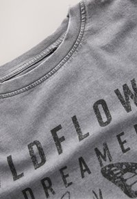 T-shirt en coton gris avec un col rond, une impression texturée et des graphiques noirs audacieux, comprenant les mots "WILDFLOWER DREAMER".