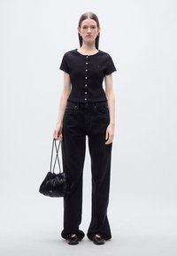 Μαύρο κοντομάνικο τοπ με κουμπιά και κυματιστά περιθώρια, σε συνδυασμό με μαύρο παντελόνι κορντό με ψηλή μέση και υφασμάτινη μαύρη τσάντα ώμου.