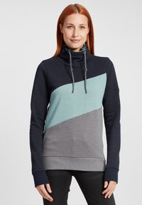 Sweat à capuche avec un col montant, présentant un design en blocs de couleur marine, turquoise et gris. Matériau texturé avec des cordons de serrage contrastés.