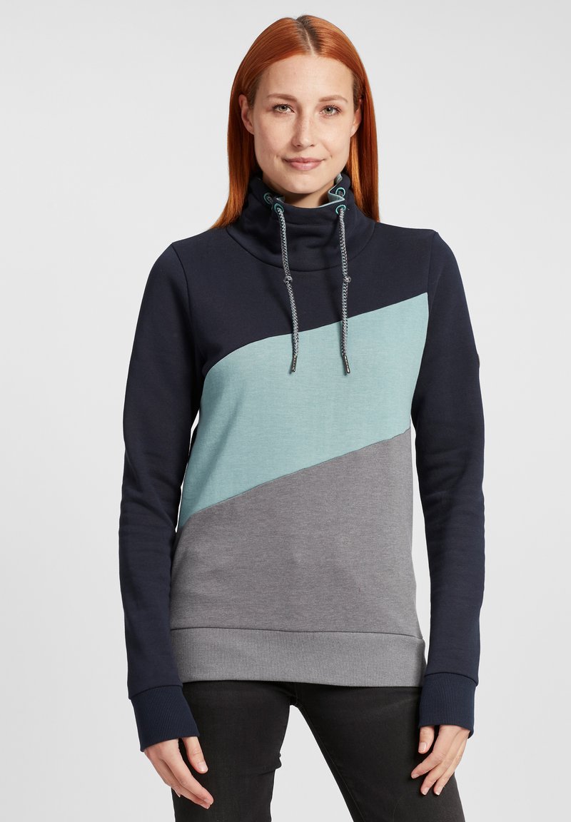 Sweat à capuche avec un col montant, présentant un design en blocs de couleur marine, turquoise et gris. Matériau texturé avec des cordons de serrage contrastés.