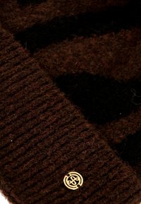 Berretto a maglia marrone con texture a coste, caratterizzato da un motivo nero e un emblema dorato sul bordo. Materiale morbido e caldo.