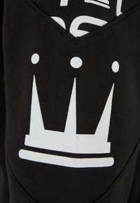 Tissu de sweat-shirt noir avec un graphique de couronne blanche à trois pointes et accents arrondis, centré sur la manche.