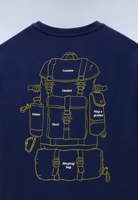 Σκούρο μπλε ύφασμα με κίτρινο σκίτσο ενός σακιδίου πλάτης με ετικέτες για θήκες κάμερας, ρούχων, φαγητού, νερού, χαρτών και υπνόσακου.