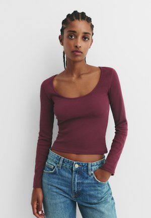 Long-sleeve, ribbed top in deep burgundy, featuring a scoop neckline, paired with high-waisted blue denim jeans.