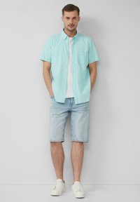 Licht turquoise kortaf sociale shirt met knopen over een wit t-shirt, gecombineerd met lichtblauwe denim shorts en witte sneakers. Geen patronen of accenten.