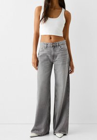 Wide-leg gray jeans made of denim, featuring a high waist, five pockets, and a button-fly closure. Paired with a white crop top.