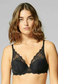 Czarny koronkowy biustonosz z falbanych brzegami, z fiszbinami i cienkimi regulowanymi ramiączkami. Materiał ma delikatny, teksturowany wzór.