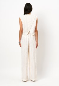 Witte jumpsuit met verticale streeptekstuur en een V-vormige rug. Beschikt over wijde pijpen en een mouwloos ontwerp. Stof heeft een iets rafelige afwerking.