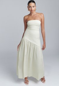Robe maxi crème sans bretelles en tissu doux. Dispose d'un haut ajusté, de coutures diagonales et d'une jupe froncée pour plus de volume.