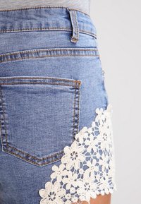 Shorts de denim en azul claro con cintura alta. Presentan un borde decorativo de encaje blanco en el dobladillo y bolsillos traseros estándar.