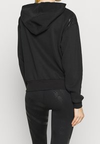 Haut de hoodie noir coupé avec capuche à cordon, texture lisse et poignets côtelés. Présente des accents brillants sur les épaules et un design ajusté.
