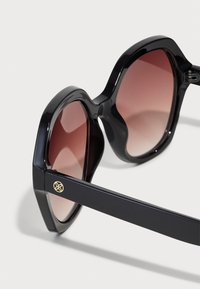 Schwarze Sonnenbrille mit einem achteckigen Rahmen, verlaufenden braunen Gläsern und einem goldenen Akzent an der Seite. Verfügt über eine glänzende Oberfläche und dicke Bügel.