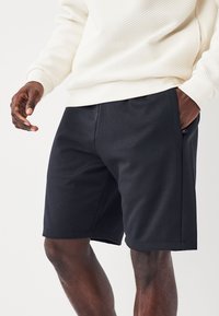 Shorts de sport noirs en tissu lisse, avec des poches latérales, une coupe droite et sans motifs ni logos visibles.