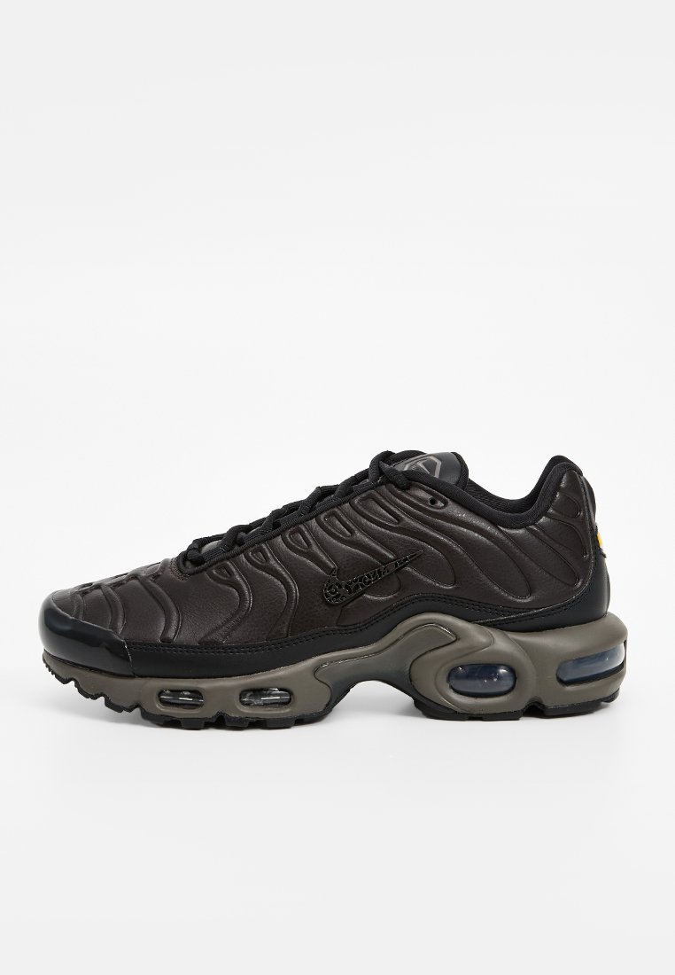 Zapatilla deportiva negra con parte superior de cuero texturizado, diseño de patrón de ondas y una gruesa suela intermedia gris con amortiguación de aire visible.