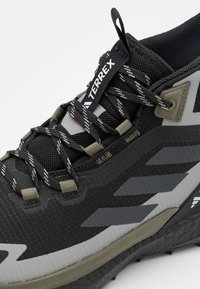 Czarno-szare buty sportowe z teksturowaną cholewką, wzmocnioną gumową podeszwą i kontrastującymi sznurowadłami, z pętlą oznaczoną napisem "TERREX".