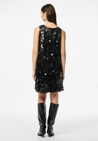 Crna haljina sa šljokicama i bez rukava, s kružnim šljokicama koje prekrivaju tkaninu. Uparena s crnim lakiranim čizmama do koljena.