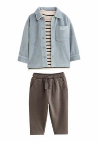 Himmelblaues Kordsakko mit einer Brusttasche über einem gestreiften Baumwolloberteil. Braune Sweatpants mit einem elastischen Bund und seitlichen Taschen.