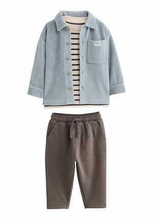 Himmelblaues Kordsakko mit einer Brusttasche über einem gestreiften Baumwolloberteil. Braune Sweatpants mit einem elastischen Bund und seitlichen Taschen.