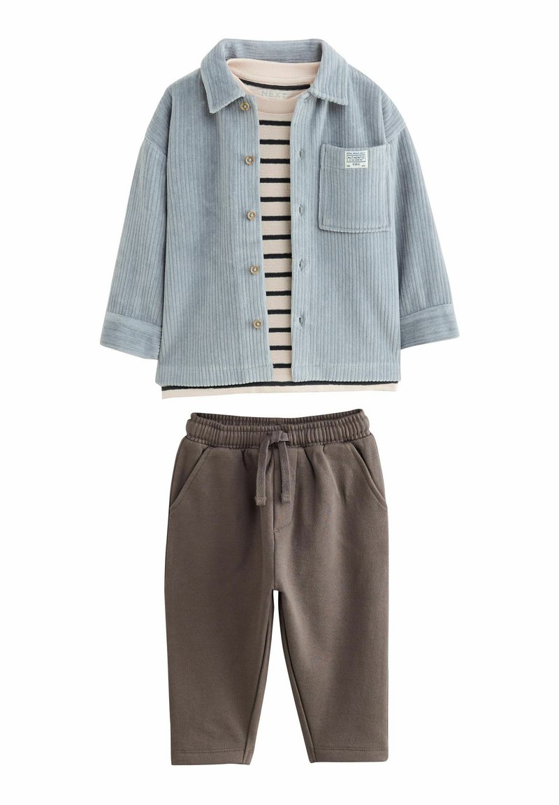 Veste chemise en velours côtelé bleu clair avec une poche poitrine sur un haut en coton rayé. Pantalons de jogging marron avec une taille élastique et des poches latérales.