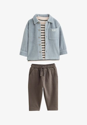 Lichtblauwe corduroy overhemdjas met een borstzak over een gestreept katoenen top. Bruine sweatpants met een elastische tailleband en zijzakken.