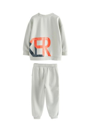 Sweatshirt gris clair et joggings assortis en tissu doux. Le sweatshirt présente un grand graphique en orange et marine, avec des épaules tombantes.