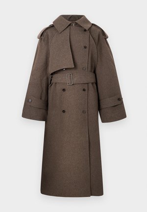 Long brown double-breasted trench coat with wide cuff straps, epaulets, waist belt, and asymmetrical storm flap on front.