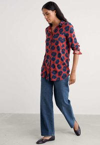 Czerwona koszula zapinana na guziki z granatowym kwiatowym wzorem, zestawiona ze luźnymi niebieskimi dżinsami i brązowymi balerinami. Subtelna faktura materiału.