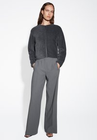 Giacca grigia in maglia con zip e collo rotondo, abbinata a pantaloni a gamba larga grigi a vita alta. Texture liscia e vestibilità rilassata.