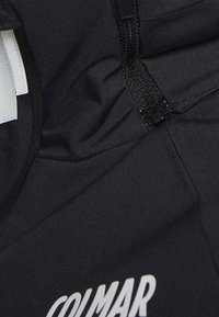 Schwarzes Kleidungsstück mit teilweise sichtbarem "COLMAR"-Logo, ausgestattet mit einem Reißverschluss und einem weißen Etikett im Kragenbereich.
